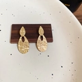 Detailansicht goldener strukturierter Doppel-Tropfenohrringe auf Holzblock-Display - Gold