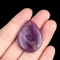 Water drop purple amethyst crystal pendant held in hand with natural stone textures - Amethyst