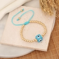 Detailed close-up of woven evil eye bracelet with gold beads and blue cord over stone - Lake Blue