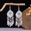 Close-up of bohemian turquoise earrings with metallic feather tassels on a wooden branch - Ancient Silver Sky Blue Turquoise Feather(E5775-20)