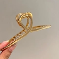 Macro view of gold metal shark hair claw showing durable spring and hollow geometric design - Gold