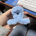 Hand holding a plush light blue faux rabbit fur hair claw clip for elegant styling - Blue