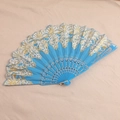 Detail of blue folding fan with gold lace patterns and sequins on a beige cloth - Light Blue