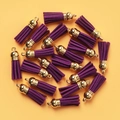 Pack of purple faux suede tassels with gold metal caps on a vibrant yellow background - Purple