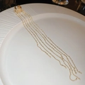 Dettaglio di ear cuff dorato con lunghe frange a catena su un piatto bianco strutturato - Pezzo Singolo / Oro