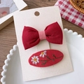 Detail of red bow hair clip and embroidered daisy hairpins on branded packaging - Embroidered Flower Group