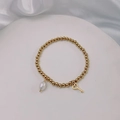 Close-up of golden beaded bracelet with pearl drop and heart key charm on white silk - Gold-Key