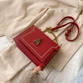 Red crossbody bee bag with gold bee buckle and chain strap on a soft beige background - Red