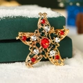 Broche étoile de Noël dorée avec strass rouges et verts sur un fond de neige douce - Étoile à Cinq Branches en Zirconium