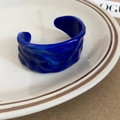 Macro detail of dark blue acrylic cuff bracelet with wavy texture on a ceramic plate - Blue