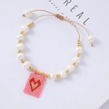 Bohemian pearl bracelet featuring golden beads and a woven pink heart pendant detail - Pink Background Red Heart