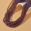 Detail of 4mm faceted purple glass spacer beads on a white stand for DIY jewelry making - Opal Grape Purple