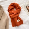 Close-up of bright orange knitted scarf with emo label on soft white linen fabric - Pumpkin Orange
