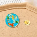 Round light blue enamel pin with goldfish and lotus leaf in a sandy gift tray - Koi Surplus Every Year