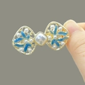 Golden bow hair clip with blue enamel petals and white pearls in a hand-held view - F1535 Bow-Blue