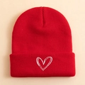 Detailed view of red ribbed knit beanie featuring white heart embroidery on the folded cuff - Red