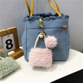 Detailed view of a pink plush mini bag keychain with pearls on a denim bag - Pink