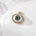 Golden Evil Eye charm with green pupil and clear rhinestones on white stone surface - Small Rhinestone Green Eye