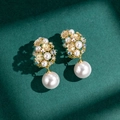 Elegante goldene Blumenohrringe mit weißen Perlen und Strass auf grünem Untergrund - Gold