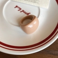 Close-up of minimalist beige resin oval ring on a white ceramic plate with red text - Brown