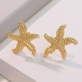 Golden starfish stud earrings with textured surface on minimalist white geometric stand - Gold Starfish Stud Earrings
