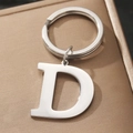 Polished silver metal letter D keychain with ring on beige textured gift box - Letter D