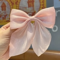 Pink bow hair clip with shimmering organza fabric texture held by hand in soft light - Korean Pink Glitter