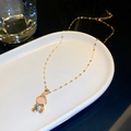 Close-up of a gold astronaut pendant with pink and blue gemstones on a ceramic tray - Astronaut Pendant (Gold)