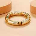 Minimalist gold curved bamboo tube bangle with high-gloss metallic finish on beige stand - Bright Gold