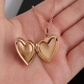 Detalle de un relicario de corazón en oro rosa abierto en una mano para ver el interior - 22.6*25mm / Oro rosa