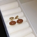 Gros plan de boucles d'oreilles ovales en résine marron dans un écrin en velours beige - Style Coeur / Café Foncé