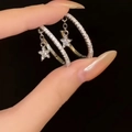 Zilveren oorringen met fonkelende zirkoon sterrenhangers gepresenteerd op een zwarte achtergrond - Zilveren Naald Creool Ster Stijl / Zilver