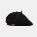 Gros plan du béret noir en maille montrant la texture fine et l'étiquette en cuir brun - Noir