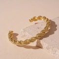 Détail d'un bracelet manchette doré torsadé posé sur un support en pierre naturelle - Or
