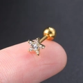 Macro-opname van een kleine gouden ster oorbel met zirkonia op een vingertop - Ster Goud - 1ST