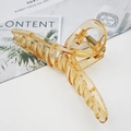 Dettaglio della grande pinza per capelli ambra con molla dorata su sfondo marmo - Arancione