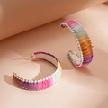 Detailed close-up of C-shaped woven earrings with colorful raffia texture and gold studs - Purple