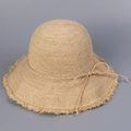 Close-up of handmade raffia sun hat with woven texture, fringed edge and straw bow - M (56-58cm) / Natural