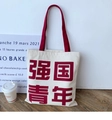 Close-up of white canvas tote bag with red handles and Chinese slogan on a wood floor - Powerful Nation Youth