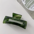 Close-up of a dark green acetate hair claw clip with a marble texture on a white surface - Rectangle