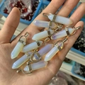Close-up of hand holding opal-like hexagonal prism pendants with silver metal clasps - Opal