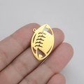 Dettaglio macro di un ciondolo a forma di rugby dorato tra le dita in primo piano - Oro