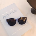 Retro lilac baby sunglasses with silver rivets and dark lenses on a blue book - Lake Blue