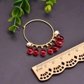 Pendientes de aro dorados con perlas blancas y gotas rojas medidos con una regla de madera - Estilo de Cristal Rojo