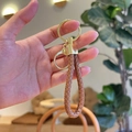 Brown braided leather keychain with golden metal ring and clasp held by hand - Brown