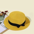 Detailed close-up of yellow straw boater hat with black ribbon bow on warm background - Yellow
