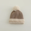 Nahaufnahme der Winter-Strickmütze mit braunem Rippmuster und flauschigem beigem Bommel - Braun