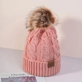Close-up of pink cable knit beanie featuring a large faux fur pompom and leather brand logo - One Size / Deep Pink