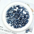 Close-up of small dark blue ceramic fish-shaped beads in a white round tray - Black