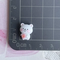 Mini statuetta di orso in resina bianca con fiore rosa mostrata con scala graduata - Orso bianco rivolto a sinistra con fiore